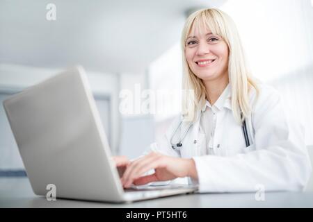 Female doctor using laptop and smiling. Stock Photo