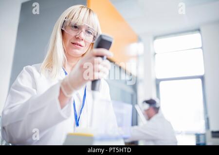 Female scientist wearing protective goggles and using device. Stock Photo