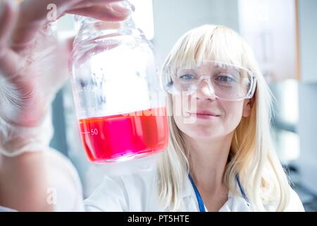 Female scientist wearing protective goggles and holding flask. Stock Photo