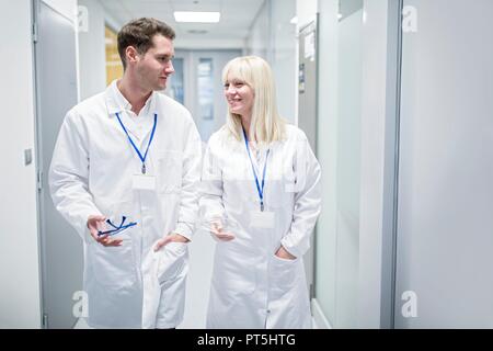 Male and female doctors in white coats walking down corridor. Stock Photo