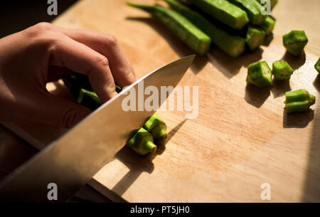 Woman cutting ladies fingers vegetable on a cutting board Stock Photo