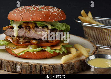 A large red burger with a piece of meat, tomatoes, pickled cucumbers, cheese, fried onion and lettuce, the sauce drains a large mouth-watering drop. Stock Photo