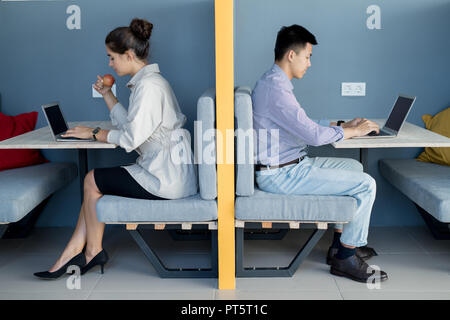 Serious busy modern freelancers in formalwear sitting at tables beyond wall and using laptops in coworking space Stock Photo