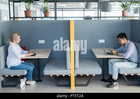 Serious young multiethnic students sitting at tables and using wireless technology in cafe Stock Photo