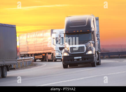 trucks goes on highway in evening on sunset Stock Photo