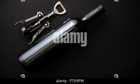 Red wine bottle and corkscrew on black matte background. Stock Photo