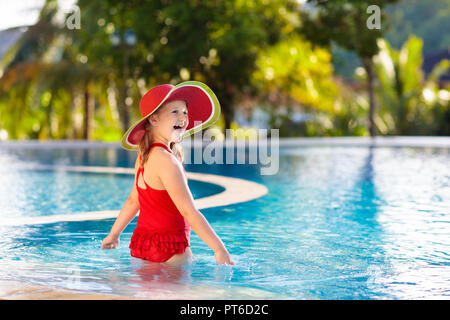 Child in swimming pool. Tropical vacation for family with kids. Little girl wearing red swimsuit and watermelon sun hat playing in outdoor pool of exo