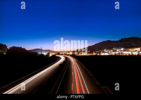 Long exposure night photography over the highway from Porto to city of Braga in Portugal. Fast car Light tracks and city lights at the dusk skyline. Stock Photo