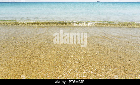 Seascape of translucent clear water shining in the sun. Yellow sand on the beach. Bright sunny day on a trip to the Greek Islands Stock Photo
