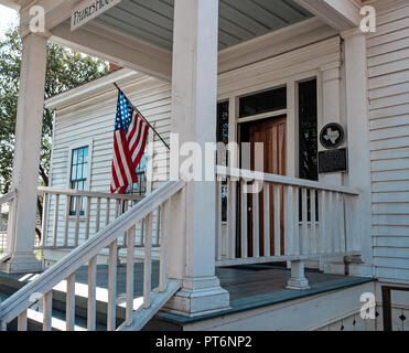 Front entrance of white shingled house with steps. Oldest standing home in Mckinney Texas, Chestnut Square. Build 1854. American flag on extended pole Stock Photo
