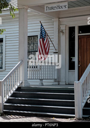 Front entrance of old, white shingled house with steps. Build 1854. American flag on extended pole. Faires  House, Chestnut Square, Mckinney Texas. Stock Photo