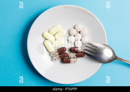 Vitamins and medicines in the form of various pills and pills on a white plate with a fork on a blue background. Stock Photo