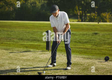 Sporty senior man teeing off with his driver while playing a round of golf on a sunny day Stock Photo