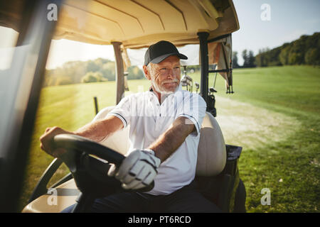 Smiling senior man driving a golf cart along a course while enjoying a round of golf on a sunny day Stock Photo