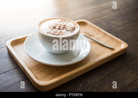 Coffee white cup with beautiful art pattern in wooden tray whute spoon on table. Select focus Stock Photo