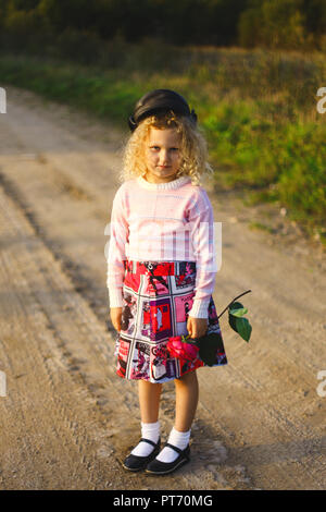 little curly blonde girl with flowers on the road Stock Photo