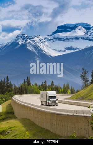 EN ROUTE REVELSTOKE TO LAKE LOUISE, AB - JUNE 2018: Large frieght truck passing snow capped mountains on the Trans Canada Highway approaching Lake Lou Stock Photo