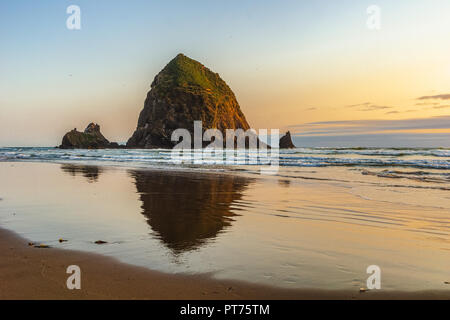 The Haystack Rock at sunset with reflection on the sandy shore, Cannon Beach, Pacific Coast, Oregon, USA. Stock Photo