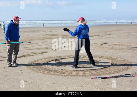 Sand artist Denny Dyke talking to a volunteer helping create a  large sand labyrinth he designed, at Heceta Beach in Florence, Oregon, USA. Stock Photo
