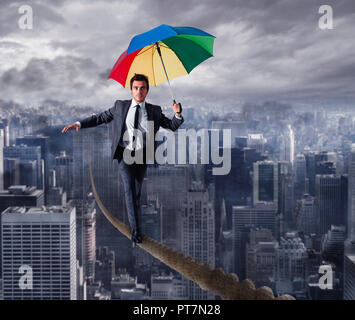 Equilibrist businessman walk on a rope with umbrella over the city. Concept of overcome the problems and positivity Stock Photo
