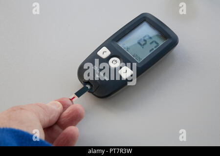 Elderley woman putting blood onto glucose test strip for read out of blood sugar levels of 6.7 checking for diabetes Stock Photo