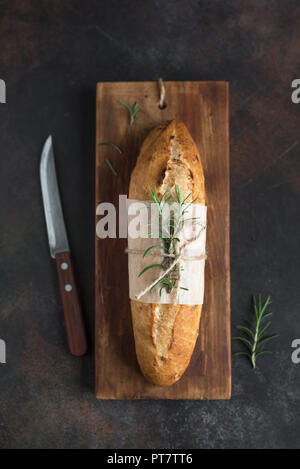 Fresh homemade bread with rosemary on rustic wooden background, top view, copy space. Sourdough mini baguette bread. Stock Photo