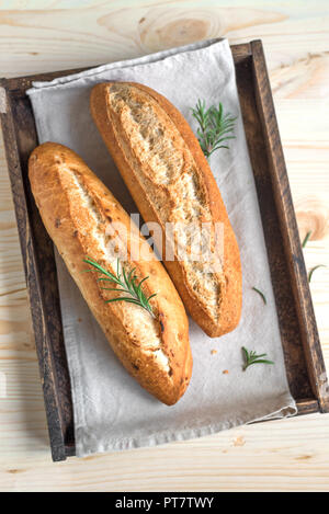 Fresh homemade bread with rosemary in rustic wooden box, top view. Sourdough mini baguette bread.
