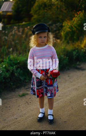 little curly blonde girl with flowers on the road Stock Photo