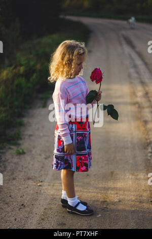 little curly blonde girl with flowers on the road Stock Photo