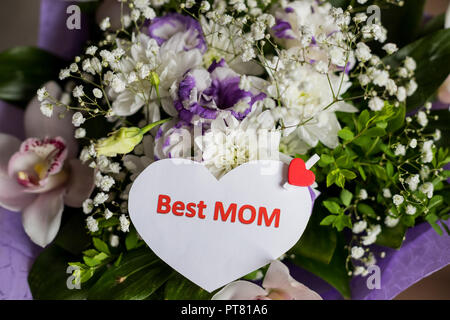 Gift tag with the text Best Mom by a bouquet of roses and a wrapped present for Mothers' Day, birthdays, and similar occasions.Lovely handwriting words. Best mom on note with hearts on floral background.Fresh branches Stock Photo