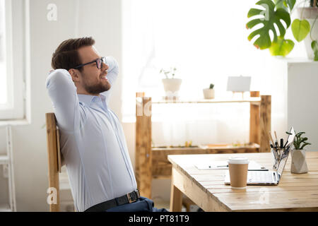 Relaxed man sitting holding hands behind head indoors Stock Photo