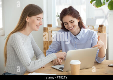 Millennial women looking at computer smiling sitting in office Stock Photo