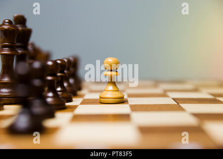 Pawn standing in front of aligned dark chess figures. Courage and leadership concept. Stock Photo