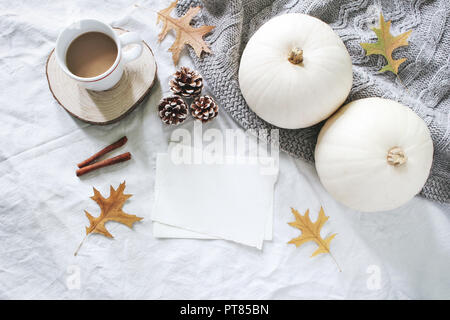 Autumn breakfast in bed composition. Blank cards mockup. Cup of coffee, white pumpkins, sweater, oak leaves and pine cones on linen background. Thanksgiving, Halloween. Flat lay. Top view. Stock Photo