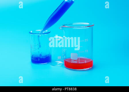 A scientist using a pipette analyzes a colored liquid to extract DNA and molecules in a laboratory glass. Pipette with blue liquid on blue background. Stock Photo