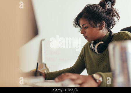 Woman making notes while working on computer. Female computer programmer working at her desk. Stock Photo