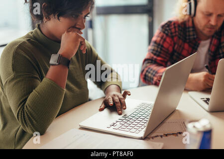 Young woman busy working on laptop at startup company. Female software engineer working on project and programming in company Stock Photo