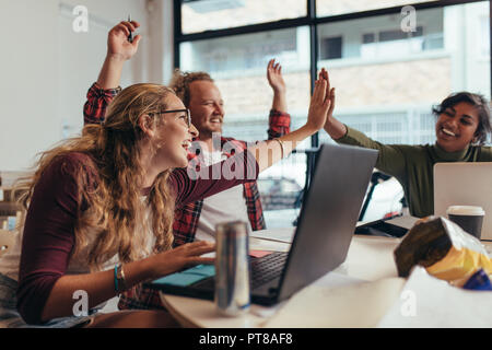 Group of young business team giving high five and celebrating success at office. Cheerful startup business team rejoicing success at office. Stock Photo