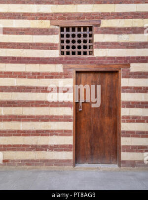 Background of old wall with red bricks and yellow stones, wooden closed door and window, Cairo, Egypt Stock Photo