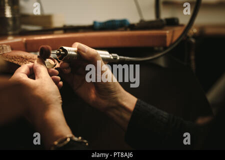Mature female jeweler polishing a gold ring at workbench. Goldsmith making a ring at her work shop using tools. Close up of hands of jewelry maker usi Stock Photo