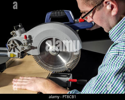 Carpenter cutting flaxboard using sliding compound mitre saw Stock Photo