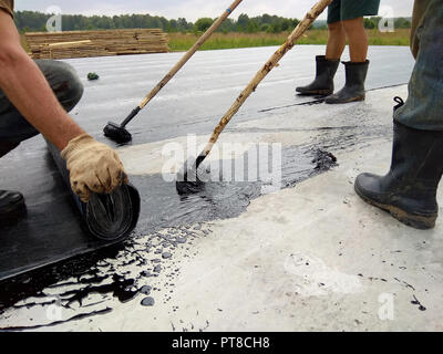 Roofer worker painting bitumen praimer at concrete surface by the roller brush Waterproofing 2018 Stock Photo