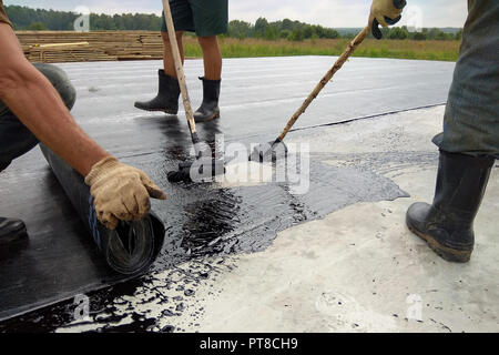 Roofer worker painting bitumen praimer at concrete surface by the roller brush Waterproofing 2018 Stock Photo