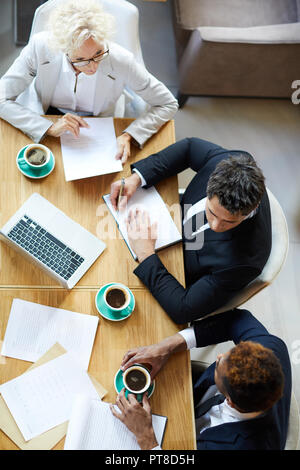 High angle view of serious thoughtful business colleagues attentively listening to African manager while they discussing project plan in restaurant Stock Photo