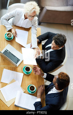 Directly above view of serious business colleagues analyzing papers and arguing about content while working in restaurant Stock Photo