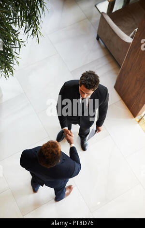 Directly above view of serious confident entrepreneurs in formal suits standing in office lobby and making handshake while greeting each other Stock Photo