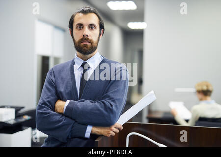 Young elegant serious businessman looking at camera while standing by tribune in conference hall or auditorium Stock Photo