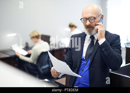 Senior speaker or professor with papers talking on smartphone to one of colleagues in auditorium Stock Photo