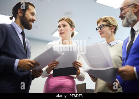 Group of young and senior speakers with papers preparing and discussing their reports before conference Stock Photo