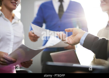 Businessman passing paper over to one of colleagues while discussing documents at meeting Stock Photo